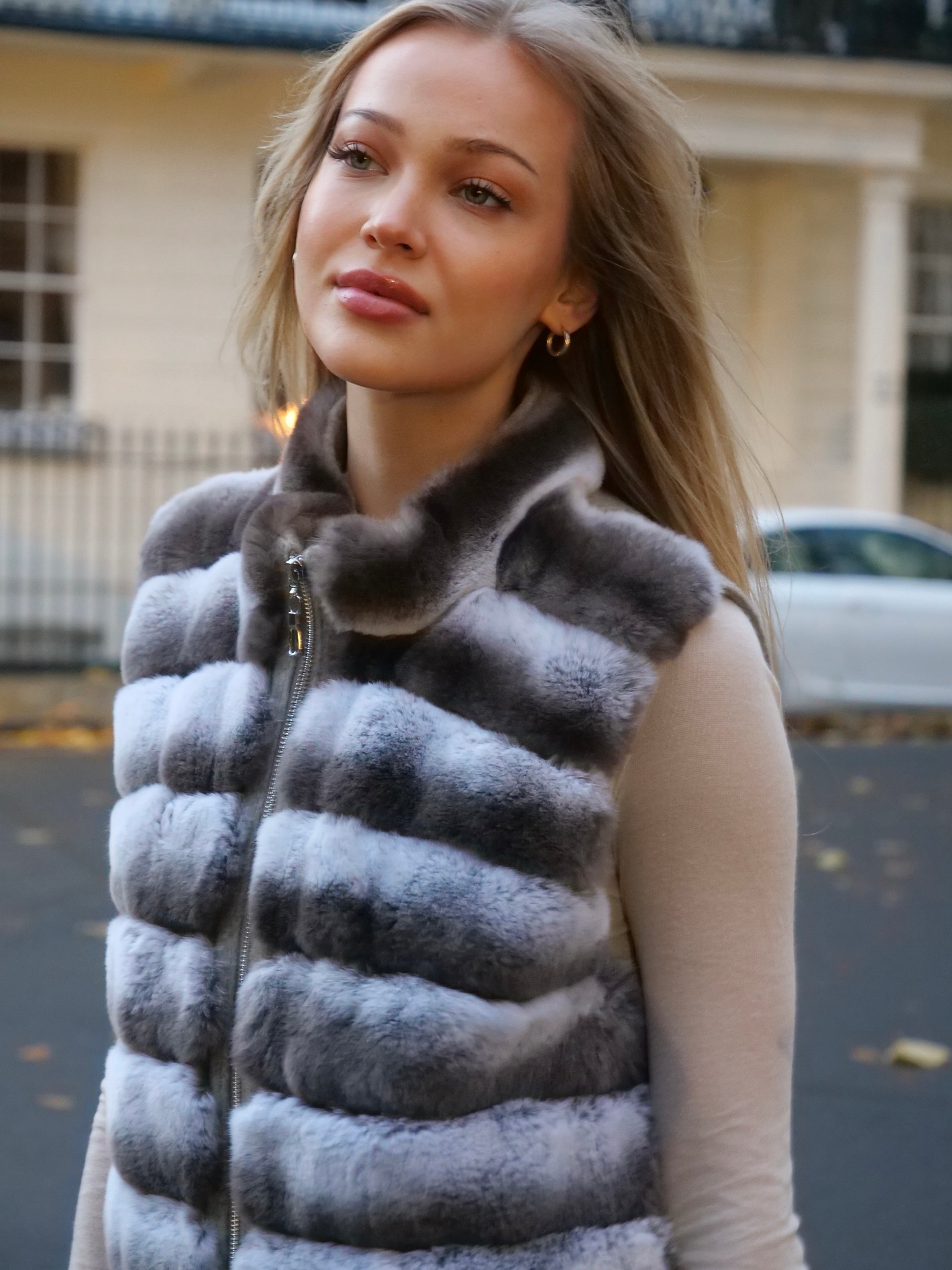 Woman wearing a grey fur vest outdoors with a blurred background