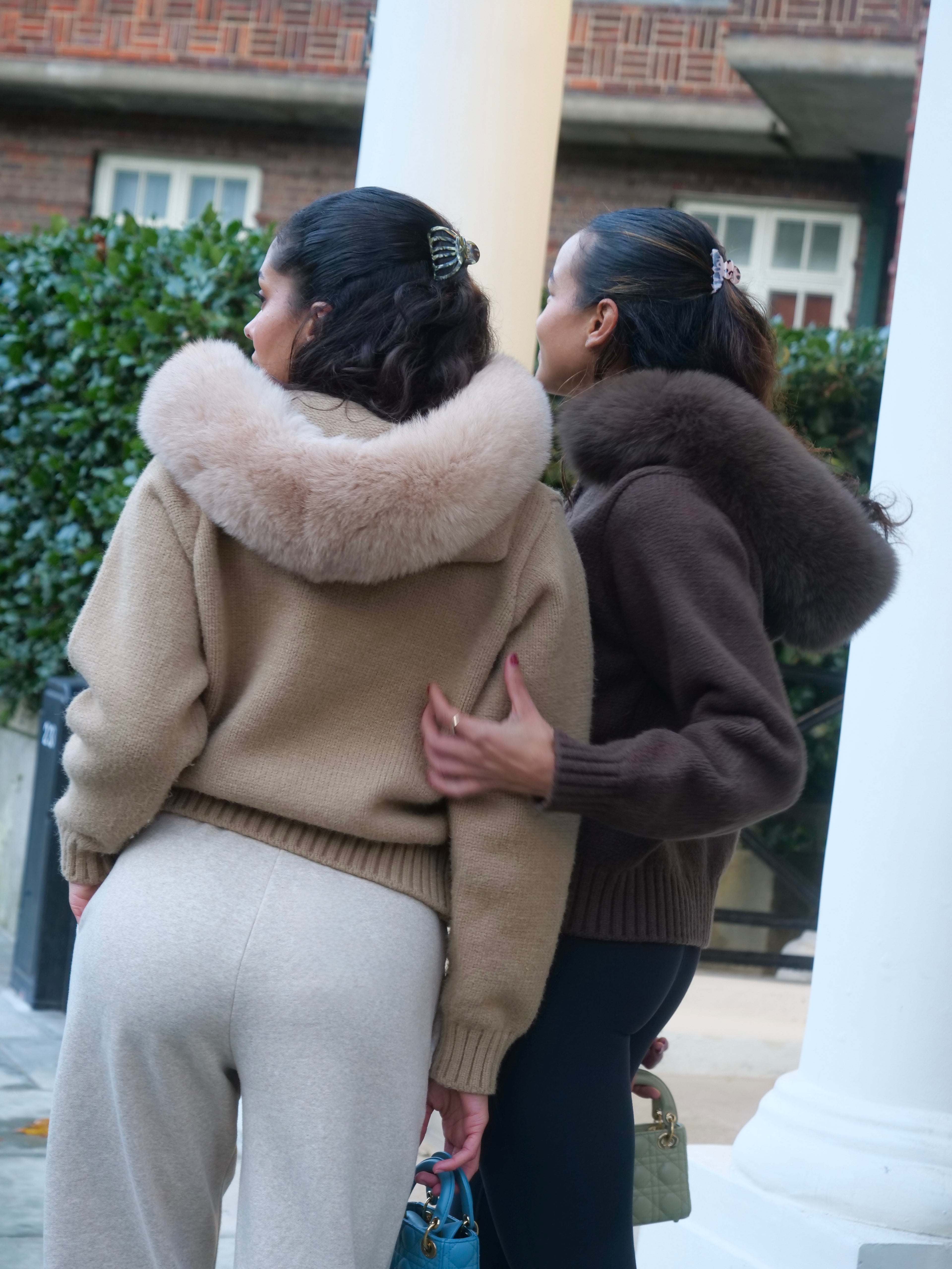 Two women hugging outdoors with a building and greenery in the background